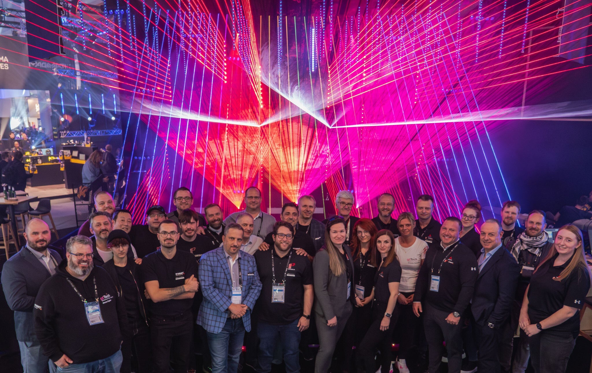 Group of people posing in front of a vibrant, abstract laser light display with red and blue hues.